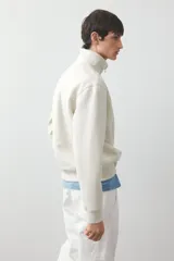 Buzo color crema de tejido pesado con interior cepillado, cuello elevado, medio cierre y hombros caídos. Puños y bajo en punto acanalado. Corte estándar.