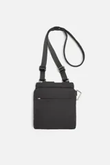 Bandolera vertical negra de tejido técnico con compartimento principal con cierre de cremallera, bolsillo interior plano y bolsillo frontal con cremallera. Incluye mosquetón y asa de hombro ajustable.