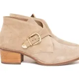 Bota corta de gamuza color avena, con diseño tipo botín chukka o desert boot modificado, que presenta una tira ancha cruzada sobre el empeine asegurada con una hebilla dorada. Posee taco bajo de madera.