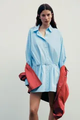 Vestido corto camisero celeste de algodón, con cuello solapa, manga larga con puños plisados, detalle de tablas en la falda y cierre frontal con botones.