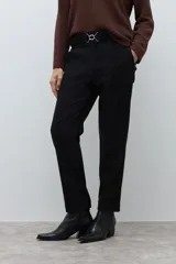 Pantalón negro de vestir, corte recto y tiro alto, con pliegues frontales y puños doblados. Se complementa con un cinturón fino negro con hebilla metálica en forma de símbolo.