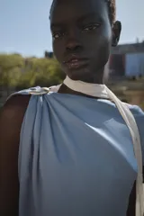 Top celeste de satén con cuello amplio, manga asimétrica y fornitura dorada en el hombro.