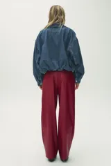Pantalón de cuero sintético color bordó, de tiro medio, corte recto y cintura cruzada con trabillas. Cuenta con bolsillos laterales, pinzas delanteras y cierre frontal con cremallera, botón y gancho metálico.