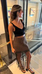 Falda corta tejida a mano en crochet, con diseño a rayas horizontales en tonos marrón oscuro y dorado brillante. Presenta un borde inferior con flecos largos y abundantes.