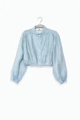 Blusa corta celeste de tejido arrugado liviano, con cuello mao, botones al frente, mangas abullonadas y ruedo elastizado.