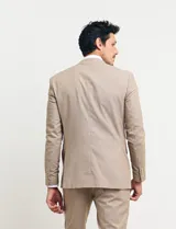 Traje de vestir color tostado, compuesto por saco con solapa de muesca, cierre de dos botones, bolsillos con solapa y pantalón de corte recto.