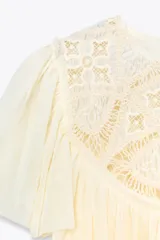 Top color crema de cuello redondo y manga corta, con detalle de bordado en el pecho y bajo con volantes. Cierre en la espalda con abertura y botón.