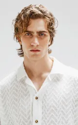Camisa blanca de manga corta con textura calada y cierre con botones marrones.
