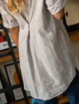 Camisa de manga larga a rayas verticales color beige y blanco, con cuello clásico, bolsillo en el pecho y cierre frontal con botones.