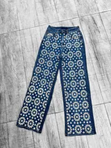 Pantalón jean azul con bordado de flores blancas.