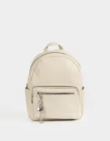 Mochila color crema de cuero sintético con bolsillo frontal con cierre y charm colgante de corazón y candado. Tiene correas regulables, manija superior, cierre superior, doble bolsillo frontal y bolsillos laterales.