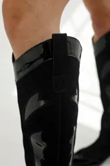 Bota bucanera negra de cuero, con detalles en charol y gamuza, diseño estilo western con punta fina y taco bajo.