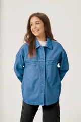 Sobrecamisa azul de jean con corte holgado, cuello camisero, cierre con botones a presión y dos bolsillos de parche en el pecho.