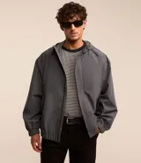 Campera gris con capucha, cuello alto, mangas largas y bolsillos con solapa y botones. Cierre frontal oculto. Marca Request, colección Primavera/Verano 2024.