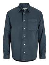 Camisa azul de manga larga con cuello clásico y cierre con botones. Tiene un bolsillo de parche en el pecho izquierdo.