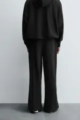 Pantalón jogger negro de corte relaxed fit, confeccionado en tejido de algodón. Presenta cintura elástica ajustable con cordón, pliegues frontales, bolsillos delanteros y un bolsillo trasero.