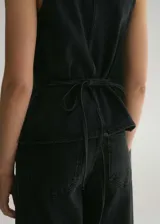 Chaleco negro de algodón estilo tejano vaquero, con cuello pico, tirantes anchos y cierre de botón en la parte delantera.