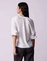 Blusa blanca de gasa marca Sioni, con cuello a la base y escote en V. Tiene abertura central con botones y mangas 3/4 con terminación fruncida.