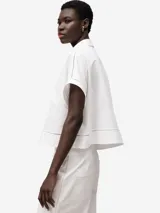 Camisa blanca de algodón con calados en el frente, ruedo y mangas. De corte recto, con cuello solapa, manga corta, botonadura frontal y bolsillo en el pecho.