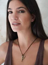 Gargantilla marrón de cuero con dije de bronce en forma de letra M.