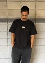 Remera negra de corte boxy con parche ovalado con texto en el frente.