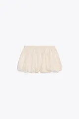 Falda pantalón corta color crudo, de tiro medio, con cintura elastizada y detalle de tejido con volumen y pliegues.
