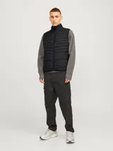Chaleco acolchado negro sin mangas con cuello alto y cierre lateral oculto y cremallera frontal. Bolsillos frontales y diseño plegable para fácil almacenamiento. Relleno de fibra sintética para calidez ligera.