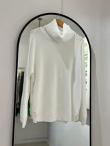 Sweater blanco de punto con cuello alto envolvente, corte recto y botones decorativos en los laterales. Detalle central tejido en espiga.