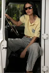 Remera tipo polo color amarillo pálido, de algodón, con cuello clásico y mangas cortas. Presenta un bordado de una rosa azul en el pecho.