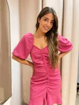 Vestido corto fucsia de crepé, con escote en V, mangas abullonadas cortas y frunce central con volados en el ruedo.