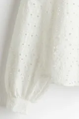 Blusa blanca de algodón con broderie, corte holgado, cuello mao con frunces, abertura en V y mangas globo largas con puños abotonados.