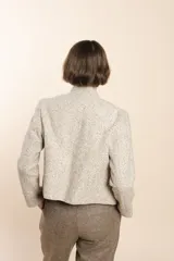 Chaqueta de sastrería color crudo con textura tweed, corte entallado, cuello mao y mangas largas.