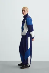 Pantalón deportivo azul marino con paneles laterales blancos y detalles en azul eléctrico. Corte relaxed fit, cintura elástica ajustable con cordón, bolsillos frontales ocultos y puños elásticos.