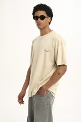 Remera color arena de corte holgado con cuello redondo y manga corta. Presenta un pequeño estampado en el frente.