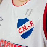 Camiseta de básquet Umbro del Club Nacional de Football. Diseño blanco con detalles en azul y rojo en cuello y sisas. Incluye logo de Umbro, escudo del club y sponsor Antel en el frente.