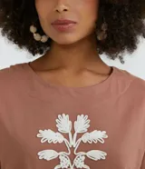Blusa color marrón claro estilo t-shirt, con cuello redondo y mangas cortas. Presenta un bordado de cocotero en el frente.