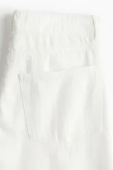 Pantalón jean blanco de tiro bajo, corte holgado en cintura y cadera, con cinco bolsillos y pierna ancha.