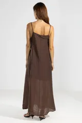 Vestido largo color marrón chocolate, con breteles finos y escote recto. Presenta lazos en los costados, forro hasta arriba de las rodillas y caída posterior más larga.
