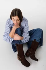 Bota de caña media color beige, de gamuza, con puntera cuadrada y taco de madera. Presenta una correa con hebilla alrededor del tobillo.