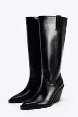 Bota alta de cuero sintético color negro, estilo cowboy, con puntera fina, tiradores laterales y tacón geométrico.