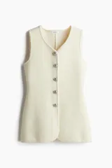 Chaleco largo color crema en punto suave de mezcla de lana. Modelo de corte entallado con ribetes tubulares, escote en V y botones de cúpula metálicos con diseño en relieve.