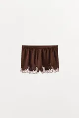 Shorts de tiro alto confeccionados en tejido satinado color marrón chocolate, con cintura elástica y detalle de bordados florales y encaje a tono en el ruedo.