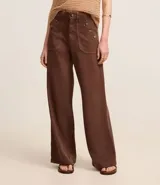 Pantalón wide leg color marrón chocolate, confeccionado en sarga de algodón y lyocell, con cintura alta, trabillas, cierre con botón y cremallera, y bolsillos tipo carpintero. Presenta botones color carey en los bolsillos delanteros.