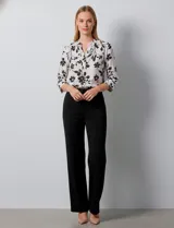 Blusa de gasa blanca con estampado floral en negro. Presenta cuello a la base con escote en V y abertura con botones. Las mangas son largas y se pueden ajustar a tres cuartos.