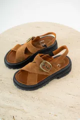 Sandalias bajas color marrón de cuero gamuzado, con tiras cruzadas y hebilla metálica.