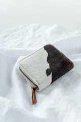 Billetera de cuero con estampado animal print de vaca en blanco y negro, con cierre de cremallera.