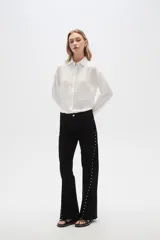 Pantalón jean negro de tiro alto, corte flare y detalle de tachas plateadas en los laterales.