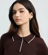 Blusa de punto color marrón, con cuello polo y ribete blanco contrastante. Tiene mangas largas y cierre frontal parcial con botones.