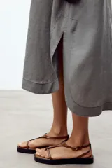 Sandalias planas color marrón con base negra, tira delantera fina y pulsera al tobillo con hebilla metálica dorada.