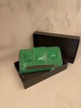 Billetera tipo clutch verde charol con cierre de cremallera y solapa con broche a presión.